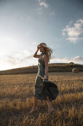 Friedliche Frau in elegantem Kleid stehend auf trockenem Feld in ländlicher Umgebung und geschlossenen Augen - ADSF25366