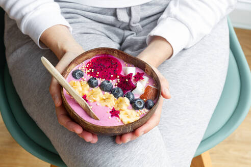 High angle of crop unrecognizable female with power bowl full of fresh banana and pitaya slices with smoothie and blueberries - ADSF25377