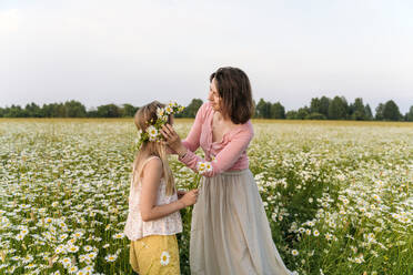 Mother making flower tiara for daughter while standing in field - EYAF01678