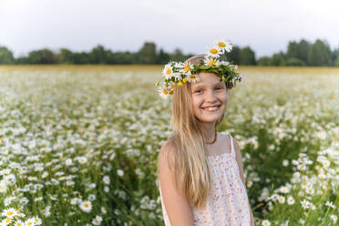Girl with chamomile tiara smiling while standing in field - EYAF01679