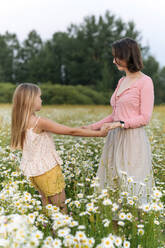 Daughter holding hands of mother while sanding at chamomile field - EYAF01684