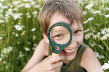 Cheerful boy looking through magnifying glass in field - EYAF01689