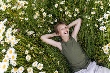 Fröhlicher Junge mit Händen hinter dem Kopf in einem Blumenfeld ruhend - EYAF01691