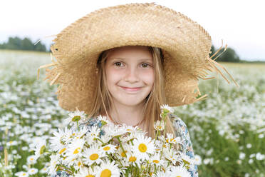 Lächelndes Mädchen mit Hut und Blumen auf einem Feld - EYAF01699