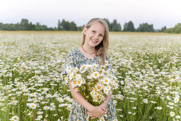 Lächelndes Mädchen hält einen Blumenstrauß auf einem Feld - EYAF01700