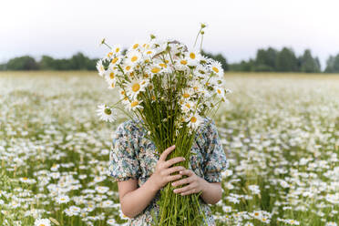 Mädchen bedeckt Gesicht mit Blumenstrauß auf einem Feld - EYAF01701