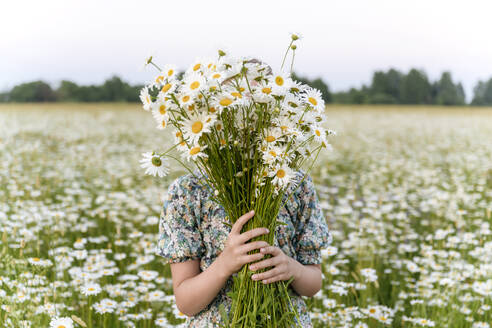 Girl covering face with bunch of flowers at field - EYAF01701