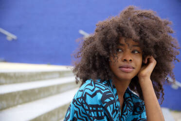 Smiling Afro woman looking away while sitting on steps - FMKF07267