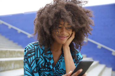 Afro woman smiling while using mobile phone - FMKF07268