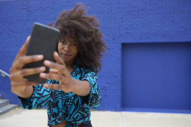 Frau nimmt Selfie durch Smartphone vor blauer Wand - FMKF07272