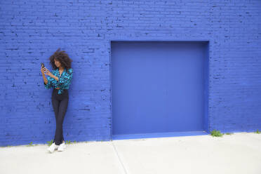 Frau benutzt Mobiltelefon vor einer Backsteinmauer - FMKF07277