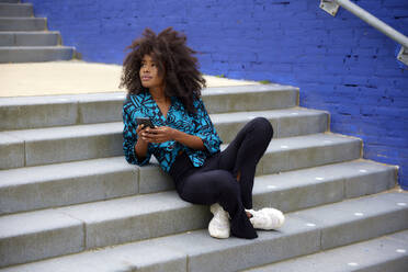 Nachdenkliche Frau mit Mobiltelefon, die sich auf einer Treppe ausruht - FMKF07284