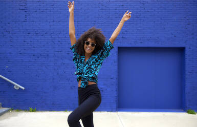 Unbekümmerte junge Afro-Frau tanzt mit erhobenen Händen - FMKF07288
