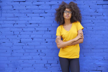 Afro-Frau mit verschränkten Armen vor einer blauen Wand stehend - FMKF07308