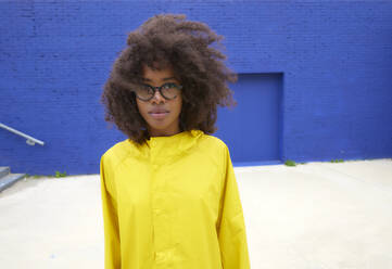 Junge Frau mit Brille steht vor einer blauen Wand - FMKF07319