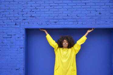 Junge Afro-Frau mit geschlossenen Augen vor einer blauen Wand - FMKF07332