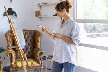 Junge Malerin betrachtet im Atelier stehend ein Bild - IFRF00904