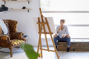 Nachdenkliche Malerin, die im Atelier sitzend ein Bild betrachtet - IFRF00905
