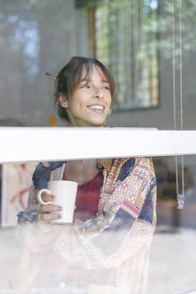 Lächelnde Malerin, die eine Tasse hält und durch ein Fenster im Atelier schaut - IFRF00928