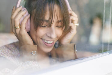 Lächelnde Frau, die über Kopfhörer Musik hört, gesehen durch ein Fenster - IFRF00929