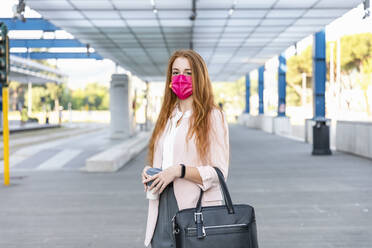 Businesswoman wearing protective face mask while standing on railroad platform - EIF01445