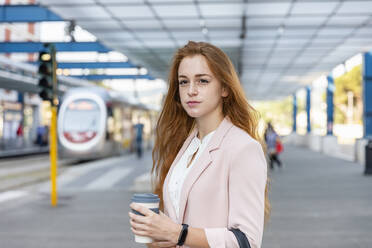 Schöne Freiberuflerin, die wegschaut und einen Einweg-Kaffeebecher auf einem Bahnsteig hält - EIF01447