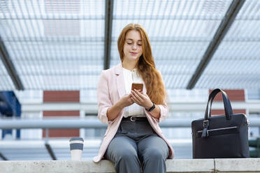 Redhead businesswoman using mobile phone on retaining wall - EIF01462