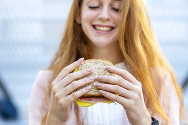Smiling redhead businesswoman having wholegrain sandwich while commuting in city - EIF01465