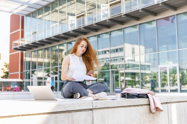 Junge Frau, die ein Mobiltelefon benutzt, während sie auf einer Bank im Büropark arbeitet - EIF01471