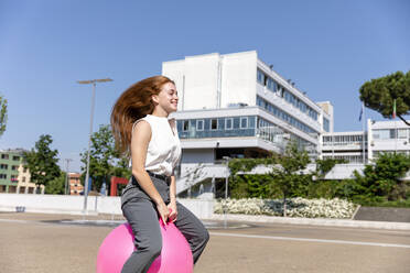 Lächelnde weibliche Freiberuflerin genießt auf Hüpfball auf der Straße während sonnigen Tag - EIF01501