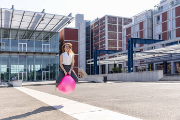 Young businesswoman looking away while jumping with bouncy ball during sunny day - EIF01504