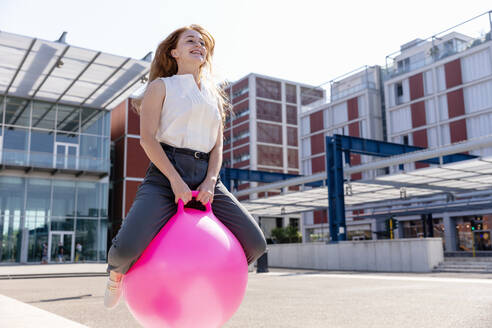 Weibliche Freiberuflerin lächelt beim Springen mit Hüpfball - EIF01506