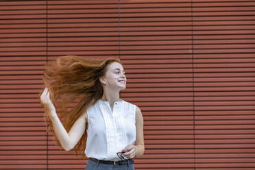 Lächelnde Frau mit zerzaustem Haar, die wegschaut, während sie vor einer Wand steht - EIF01513