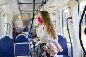 Rothaarige Geschäftsfrau mit Jacke und Einweg-Kaffeebecher schaut weg, während sie im Zug steht - EIF01523