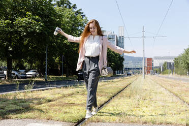 Businesswoman with arms outstretched balancing on railroad track during sunny day - EIF01530