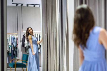 Frau schaut in den Spiegel und trägt ein blaues Kleid in einer Boutique - EIF01563