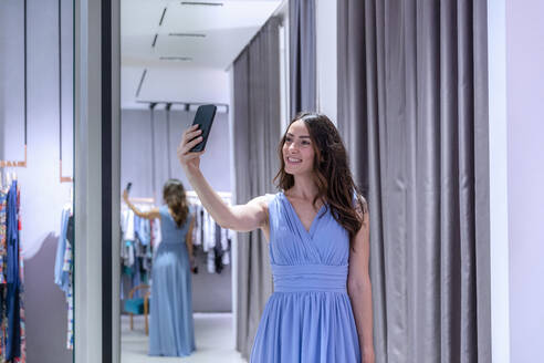 Frau macht Selfie im blauen Kleid in der Nähe der Umkleidekabine einer Boutique - EIF01566