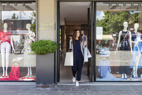 Woman holding shopping bags while walking out from boutique - EIF01576