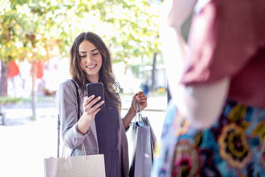 Smiling woman using smart phone while holding shopping bags - EIF01580