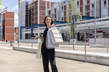 Woman looking away while standing with shopping bags in city - EIF01586