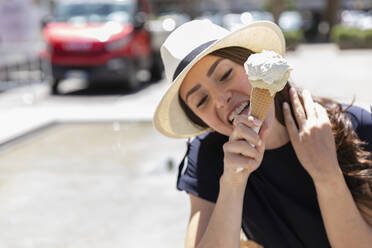 Woman in sun hat licking ice cream - EIF01615