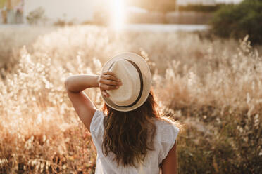 Woman wearing hat while standing in field during sunset - EBBF04192