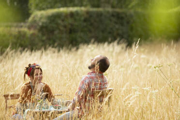 Glückliches Paar lachend am Tisch in einem sonnigen Feld mit hohem Gras - CAIF30848