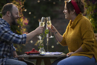 Happy couple enjoying champagne and red currants at patio table - CAIF30854