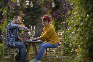 Couple enjoying champagne and red currants at table in garden - CAIF30856