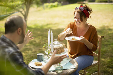 Glückliches Paar genießt Kuchen und Tee am sonnigen Gartentisch - CAIF30858