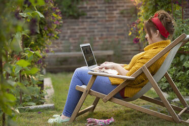 Frau arbeitet am Laptop im Garten - CAIF30860