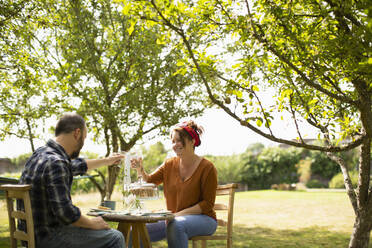 Happy couple toasting water glasses at table in sunny summer garden - CAIF30869