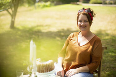 Porträt einer glücklichen Frau, die am Tisch im sonnigen Sommergarten Kuchen genießt - CAIF30871