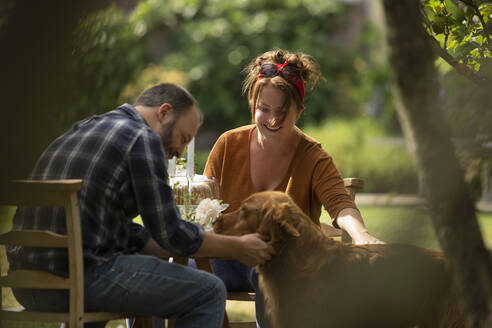 Happy couple with Golden Retriever dog at garden table - CAIF30872